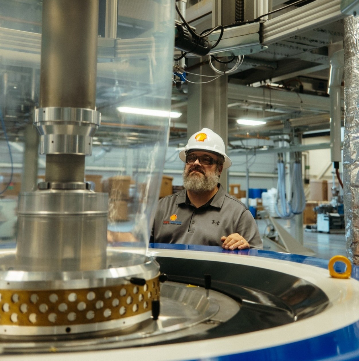 Shell Polymers employee wearing hard hat and safety glasses watches plastic machine